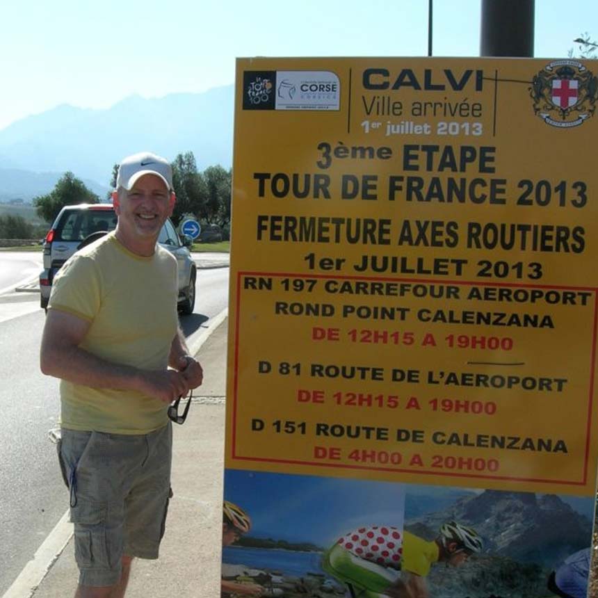 Cyclist beside a Tour de France 2013 stage sign in Calvi, Corsica